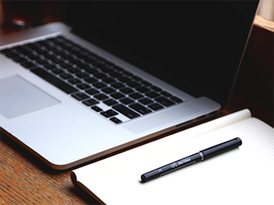 Decorative photo of a laptop with a pen and notepad next to it